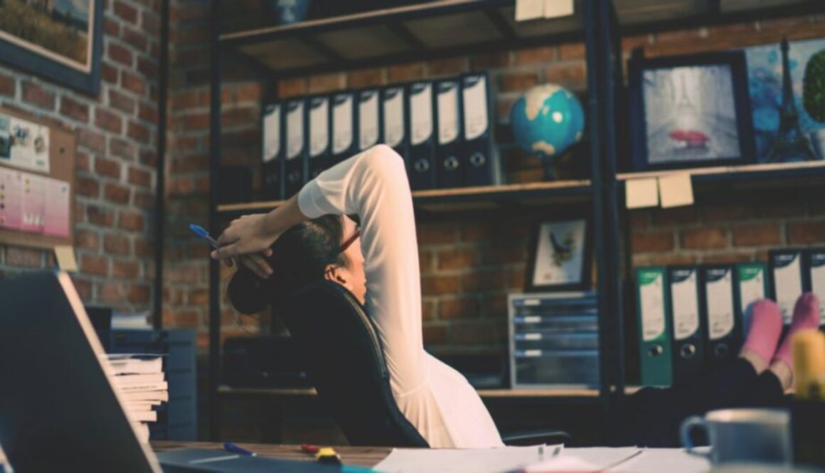 Woman at a desk leaning back in a chair with her feet up on a table while turning her back on her laptop.