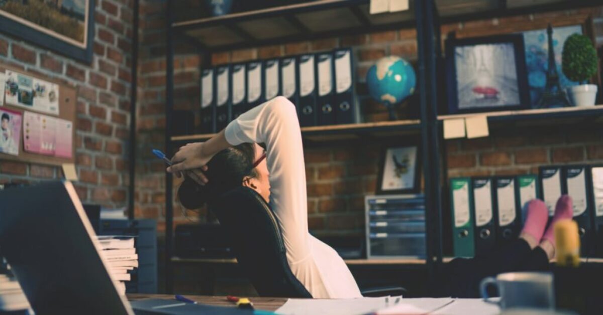 Woman at a desk leaning back in a chair with her feet up on a table while turning her back on her laptop.