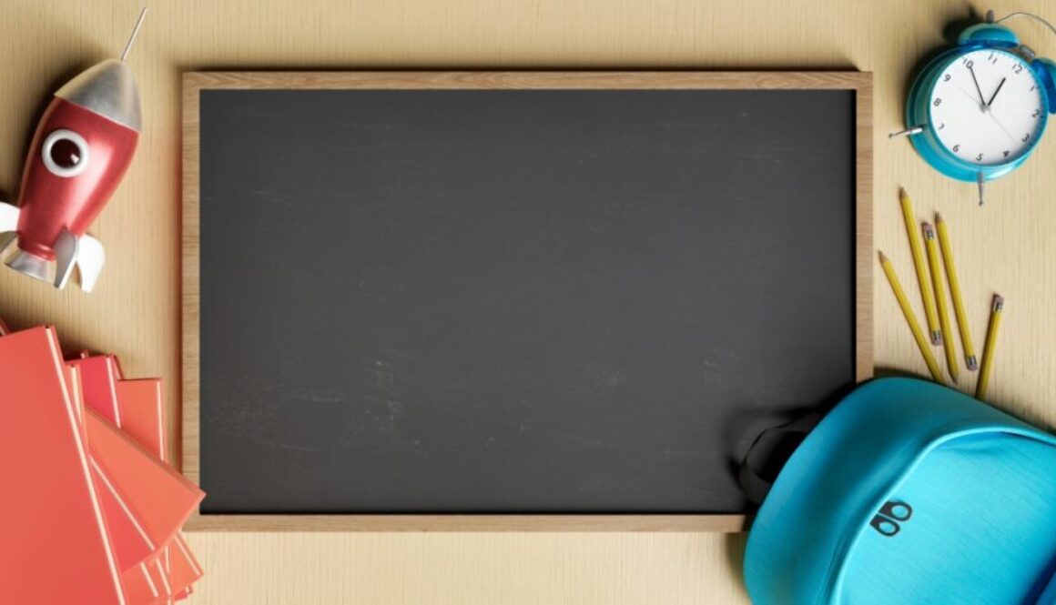 A blank chalkboard surrounded by school supplies, a toy space ship and alarm clock.