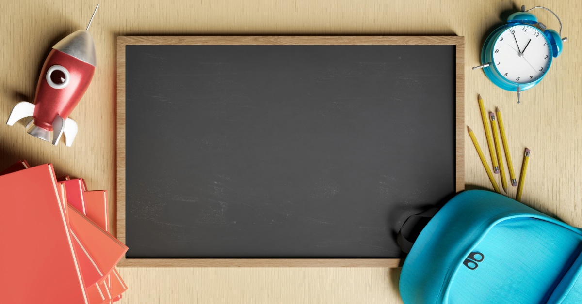 A blank chalkboard surrounded by school supplies, a toy space ship and alarm clock.
