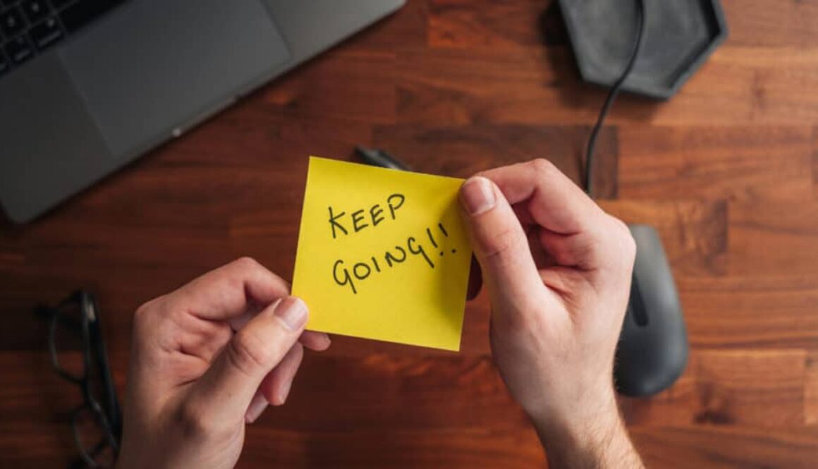 a person holding a yellow note with the words keep going