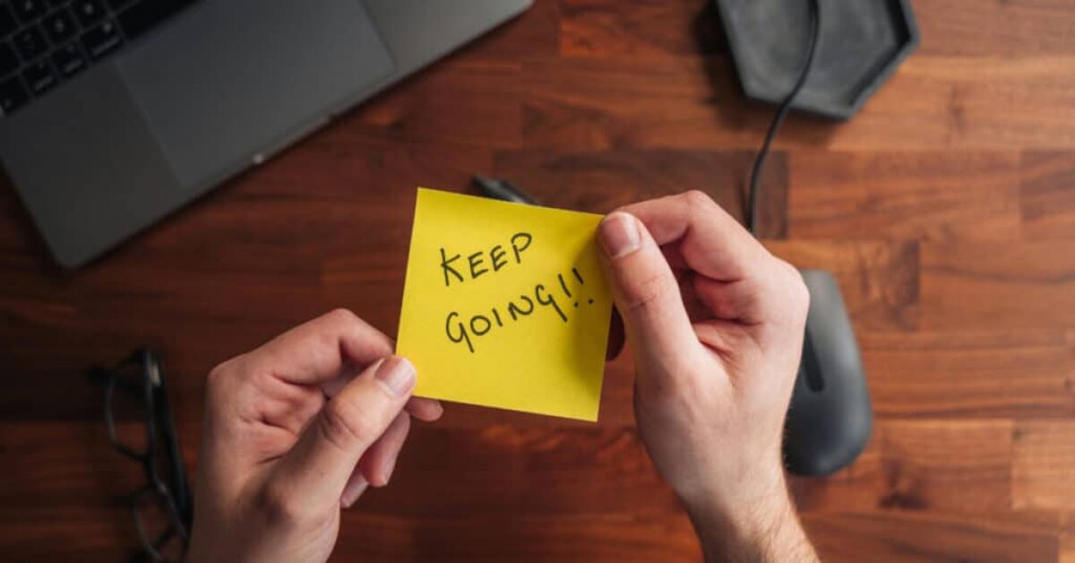 a person holding a yellow note with the words keep going