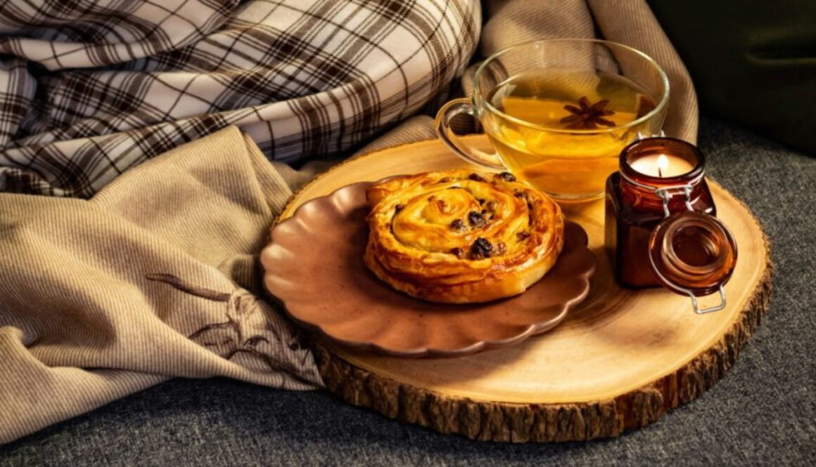 a cup of tea, a raisin bun and a candle beside blanket