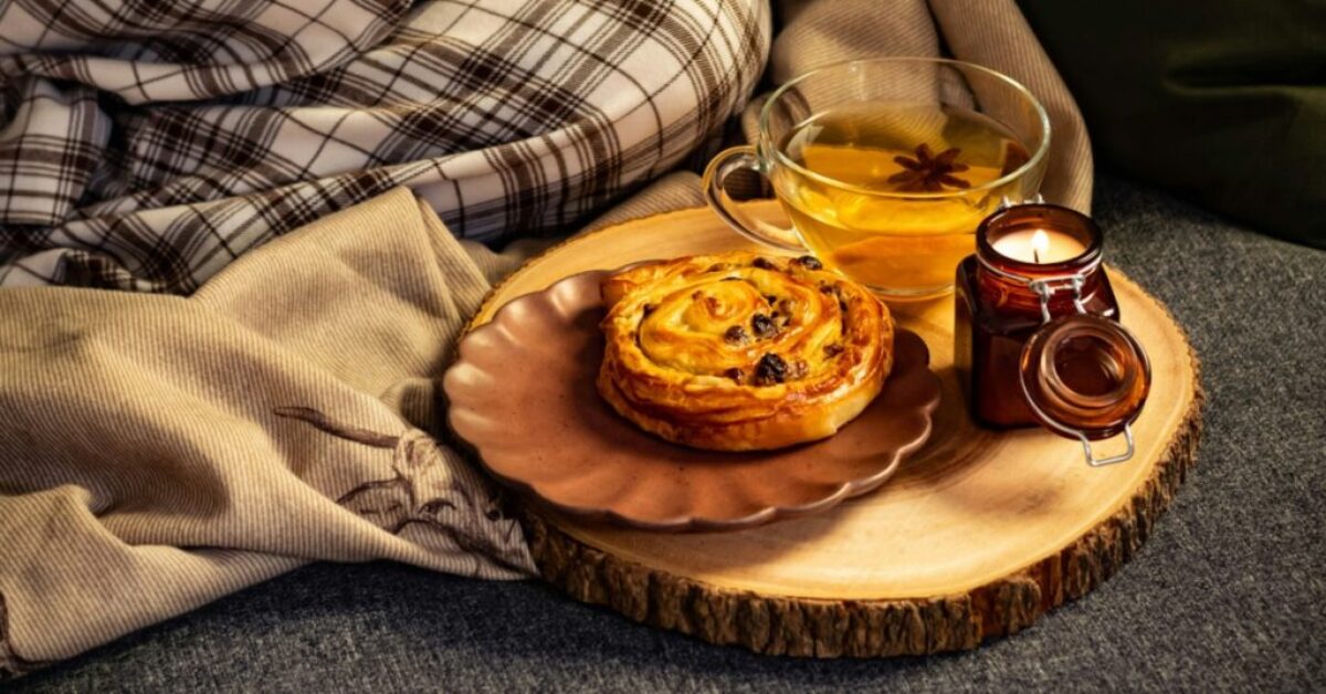 a cup of tea, a raisin bun and a candle beside blanket