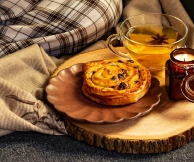 a cup of tea, a raisin bun and a candle beside blanket