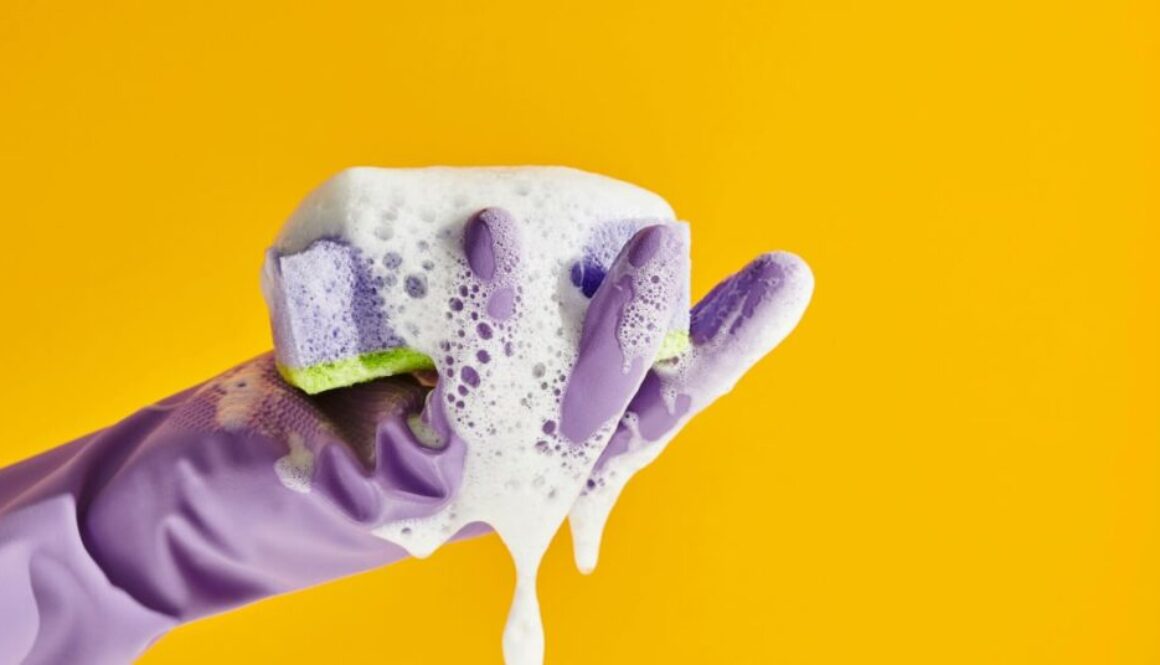 a hand wearing a rubber glove holding a soapy sponger
