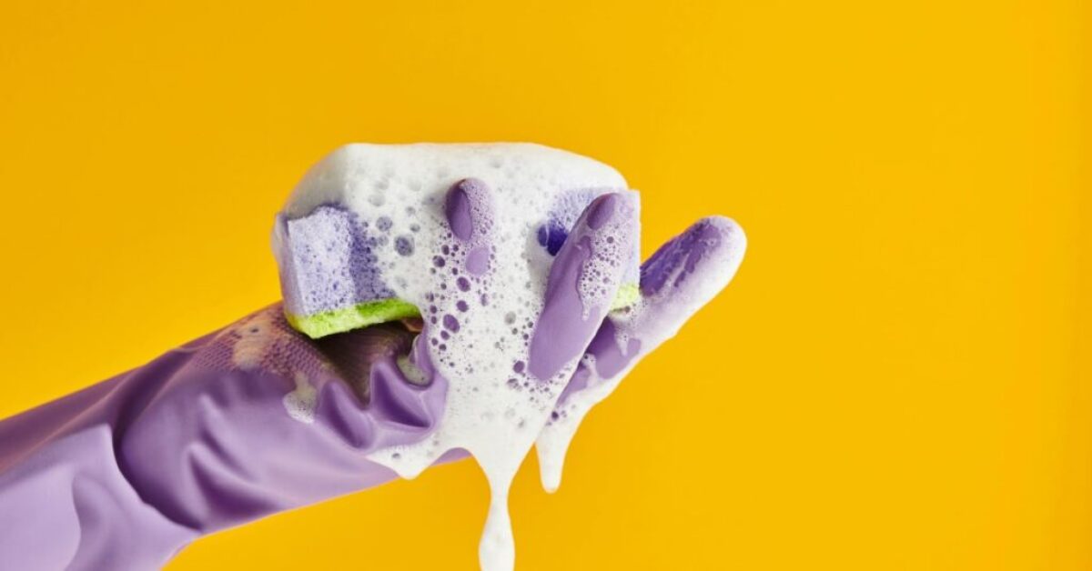 a hand wearing a rubber glove holding a soapy sponger