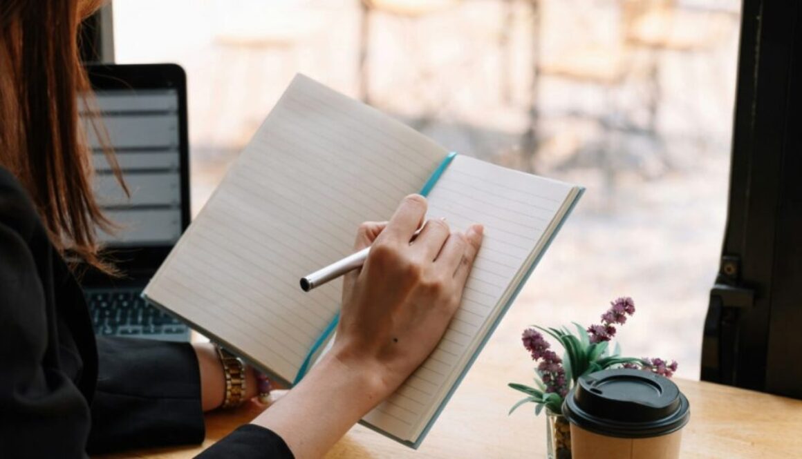 a woman sits at a desk with a cup of coffee and writes in a notebook