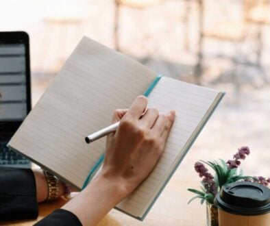 a woman sits at a desk with a cup of coffee and writes in a notebook