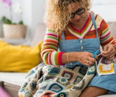 a woman sits on a couch and crochets a blanket